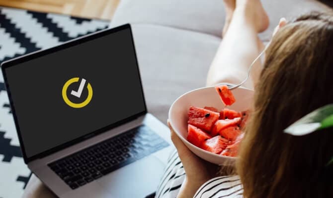 Mujer comiendo frutas junto a una computadora portátil abierta